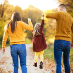 Family walking hand-in-hand through a scenic forest trail during autumn, symbolizing the joy and connection of affordable family vacations in nature.
