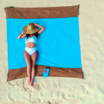A woman relaxing on a beach towel, wearing a white swimsuit and a wide-brimmed hat, enjoying the serene beach setting.