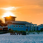 A breathtaking sunset over beachfront properties and hotels in Panama City Beach, with white sand, cozy beach houses, and golden skies creating the perfect vacation vibe.